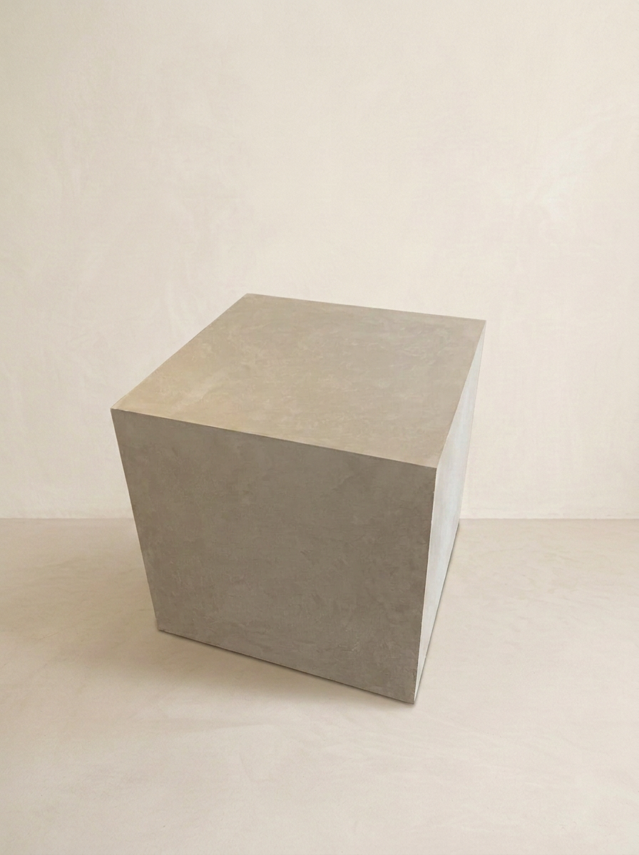 Grey hand-trowelled microcement cube side table in a plaster-walled studio
